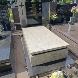 Kamil Jaszczyński - Jasny, prostokątny element z kamienia o wzorze trawertynu, na ciemnej, polerowanej podstawie. W tle czarna płyta z grawerem i złotym krzyżem, znicze i żółto-białe kwiaty.