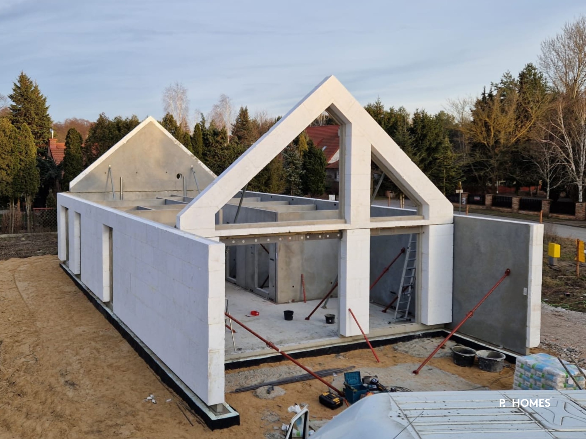 Surowy stan modułowego domu P.Homes w trakcie budowy, z widocznymi ścianami z izolacją, wzmocnieniami i elementami konstrukcyjnymi na tle drzew i nieba.