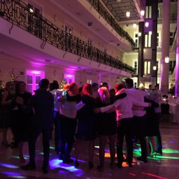 Dj Monde - Rozświetlona sala balowa w Warszawie z bawiącymi się ludźmi, oświetlenie sceniczne i dekoracje świąteczne tworzą radosny nastrój.