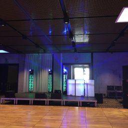 Dj Monde - Scena z nagłośnieniem i oświetleniem w sali balowej. Widoczne kolumny głośnikowe, oświetlenie sceniczne i biały parawan DJ-a. Parkiet taneczny.