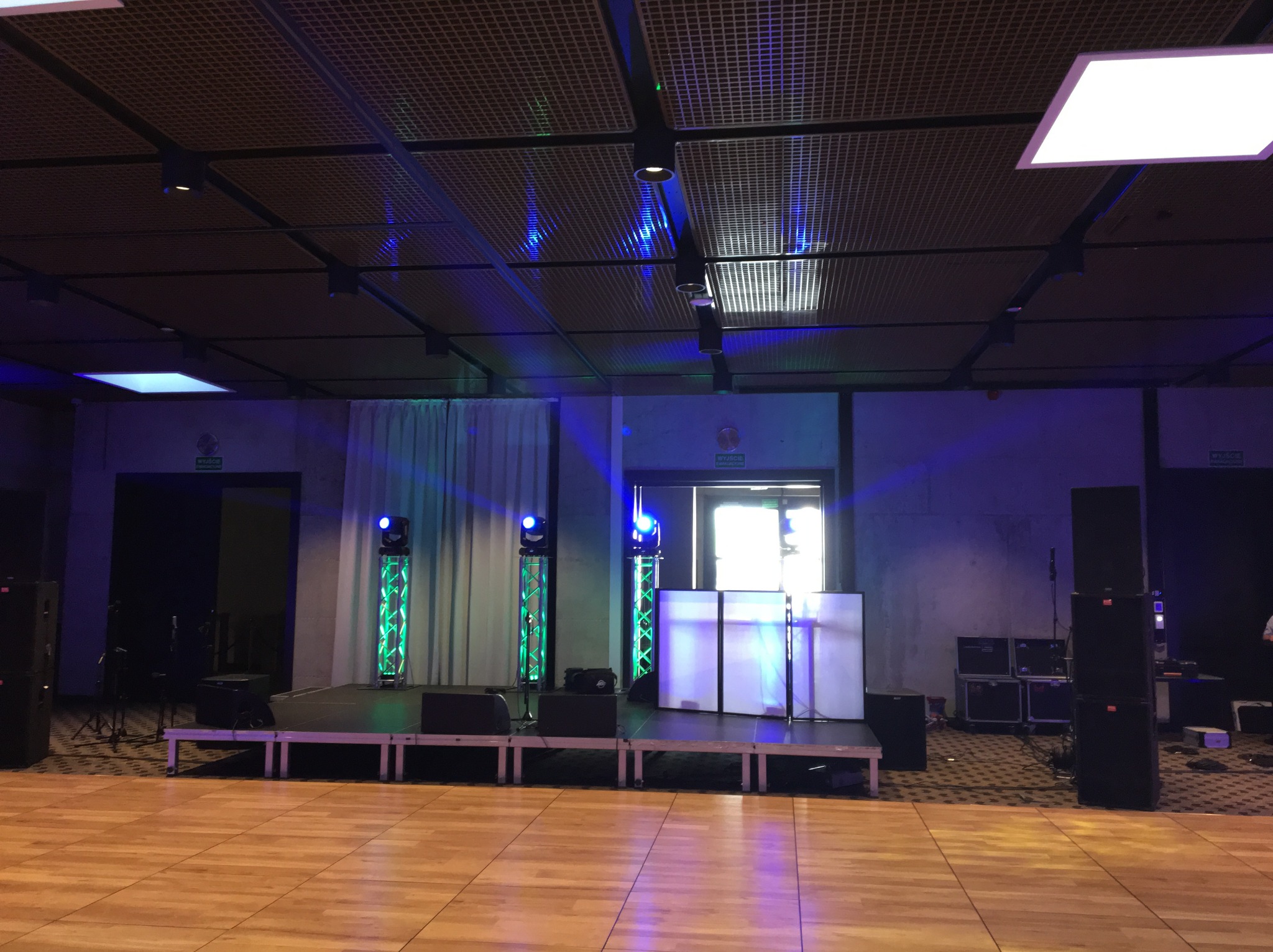 Scena z nagłośnieniem i oświetleniem w sali balowej. Widoczne kolumny głośnikowe, oświetlenie sceniczne i biały parawan DJ-a. Parkiet taneczny.