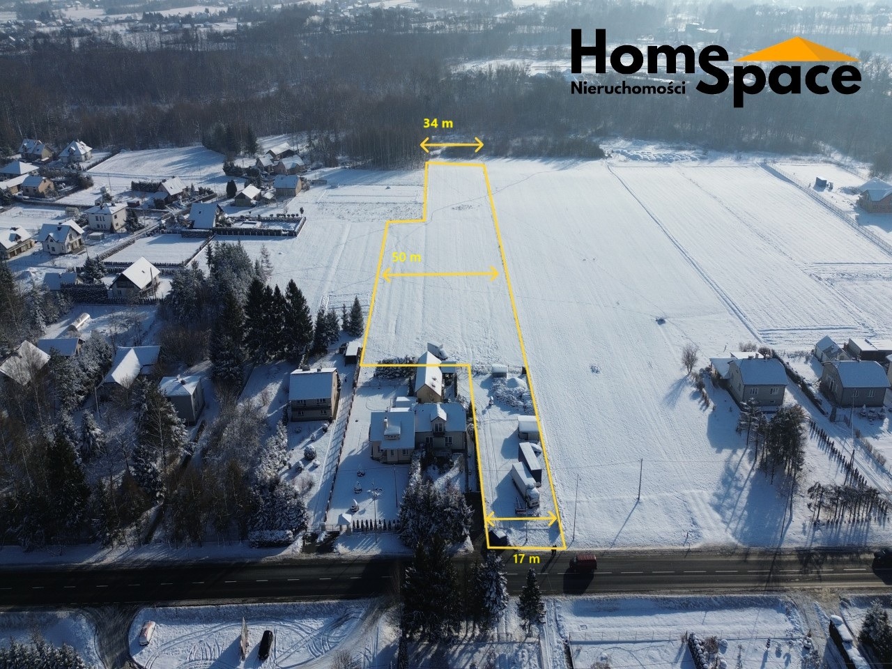 Zimowy widok z lotu ptaka na działkę z naniesionymi wymiarami (34m, 50m, 17m) w żółtych liniach. W tle zabudowa jednorodzinna i logo Home Space Nieruchomości.