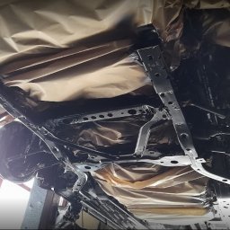 RAJAUTO CENTER ANDRZEJ MAGACZEWSKI - Podwozie samochodu po konserwacji antykorozyjnej, zabezpieczone papierem maskującym, widoczne elementy zawieszenia i układu kierowniczego pomalowane na czarno.