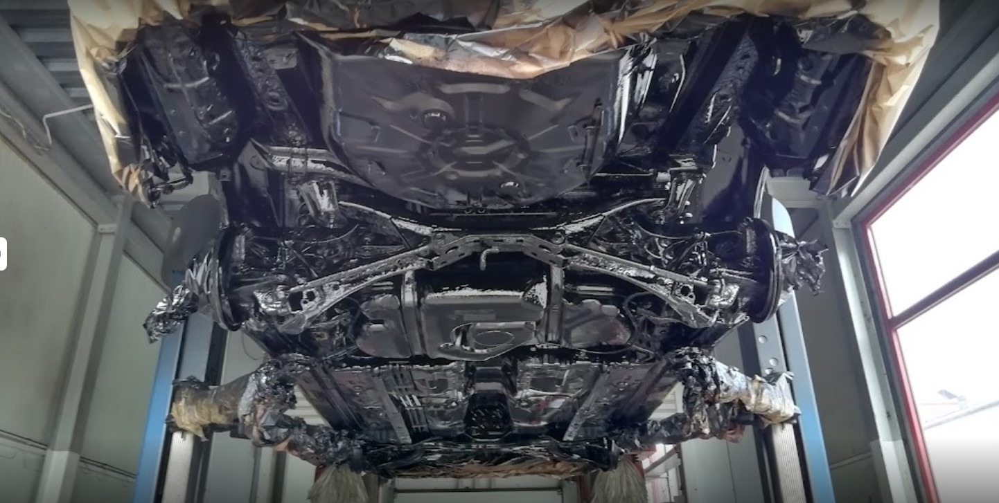 Podwozie samochodu po konserwacji antykorozyjnej, widok od dołu na podnośniku. Elementy zawieszenia i karoserii pokryte czarną, błyszczącą powłoką ochronną.