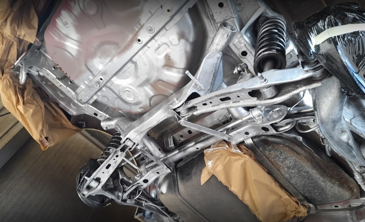 Podwozie auta po konserwacji antykorozyjnej, widoczne elementy zawieszenia i układu wydechowego zabezpieczone papierem. Świeża, srebrna powłoka ochronna.