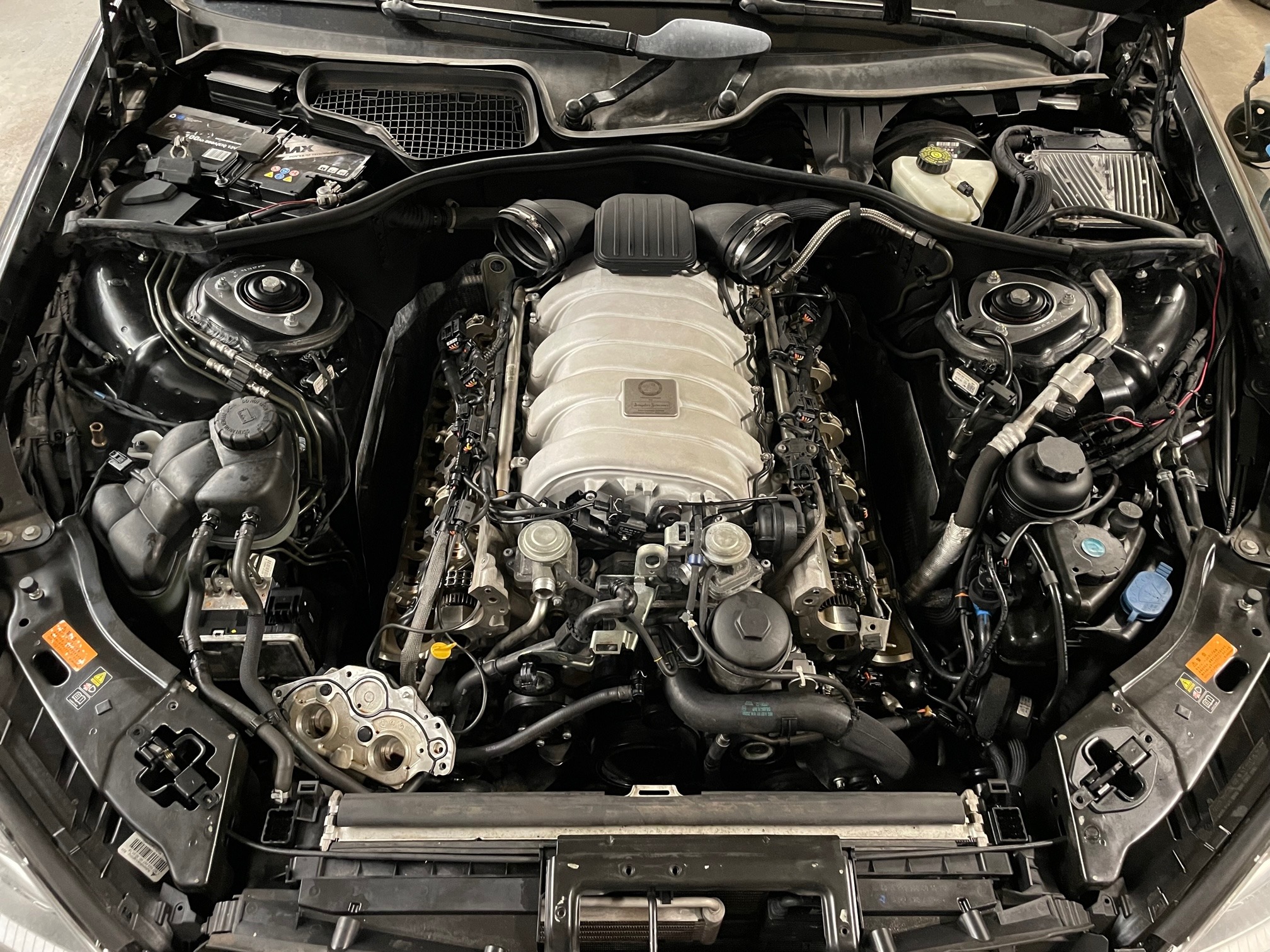 Otwarty silnik samochodu w warsztacie. Widoczne elementy mechaniczne, przewody i osprzęt. Detaliczny widok na skomplikowaną konstrukcję silnika spalinowego.