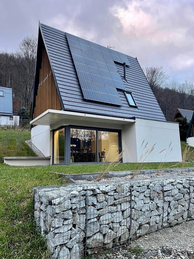 Nowoczesny, całoroczny domek letniskowy z panelami słonecznymi na dachu i kamiennym murkiem oporowym z przodu, Radków.