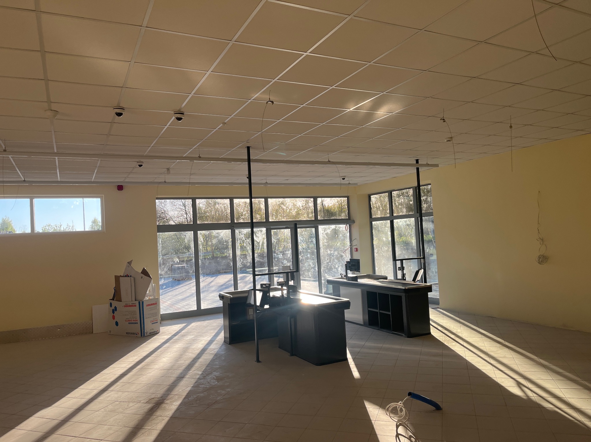 Jasne wnętrze sklepu po remoncie z kasami, oświetleniem sufitowym i systemem kamer monitoringu. Promienie słoneczne wpadają przez okna.