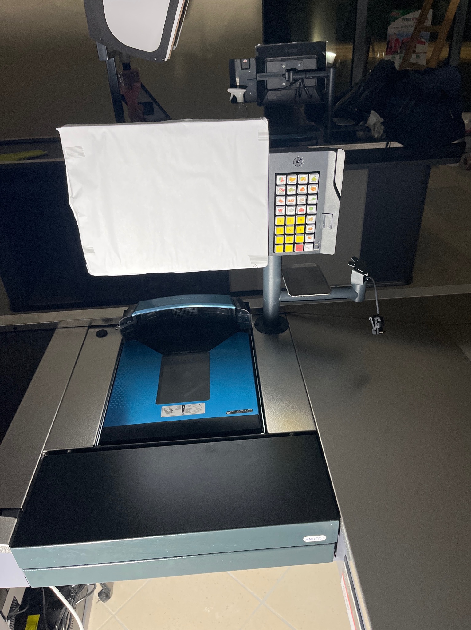 Stanowisko kasowe z czytnikiem kodów kreskowych i panelem dotykowym, oświetlone studyjną lampą. Widoczny skaner i klawiatura numeryczna.