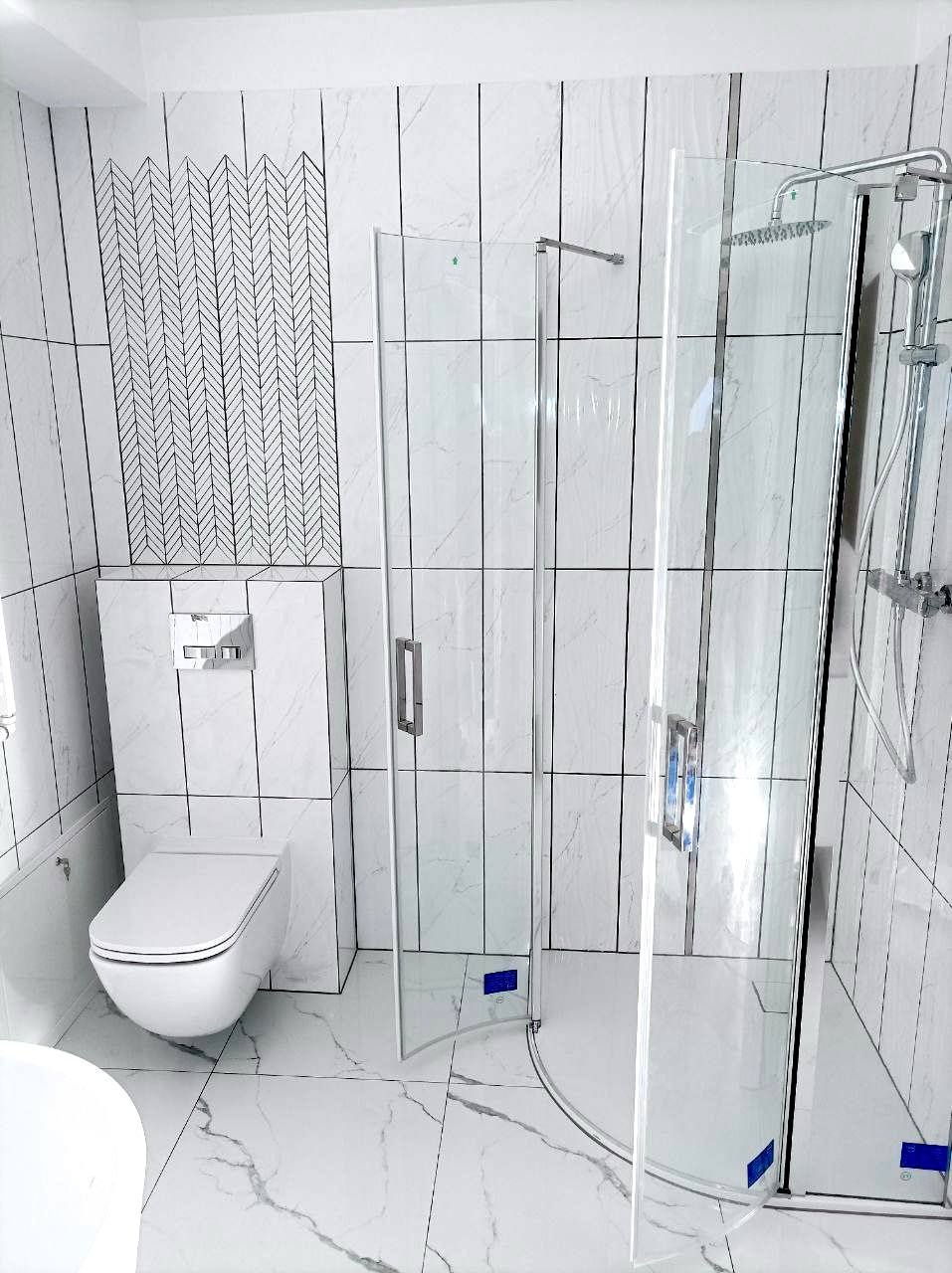 Nowoczesna łazienka z kabiną prysznicową, białą armaturą i oryginalną mozaiką na ścianie, imitującą jodełkę. Płytki imitujące marmur na podłodze i ścianach.