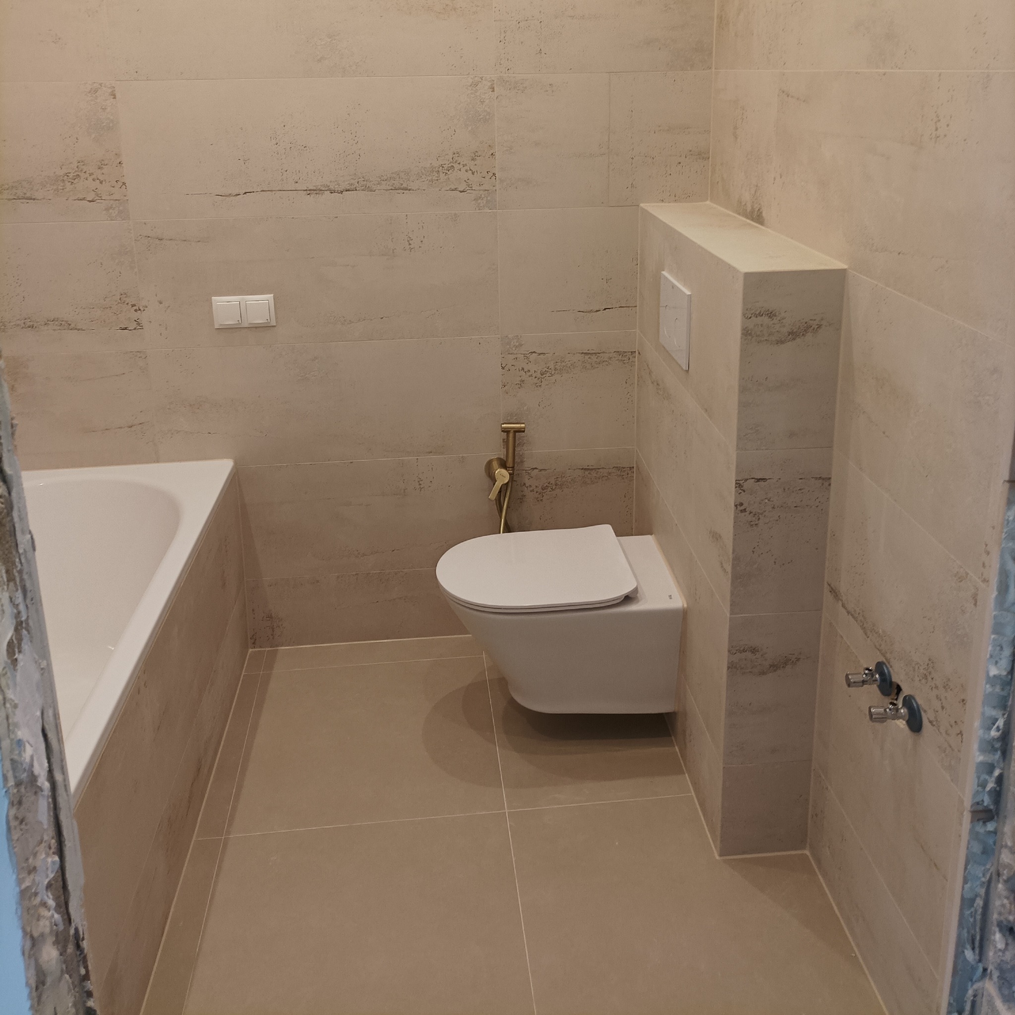 Nowoczesna łazienka w beżach: podwieszana toaleta z bidetką, płytki imitujące kamień na ścianach i podłodze, zabudowa geberitu. Minimalistyczny design.