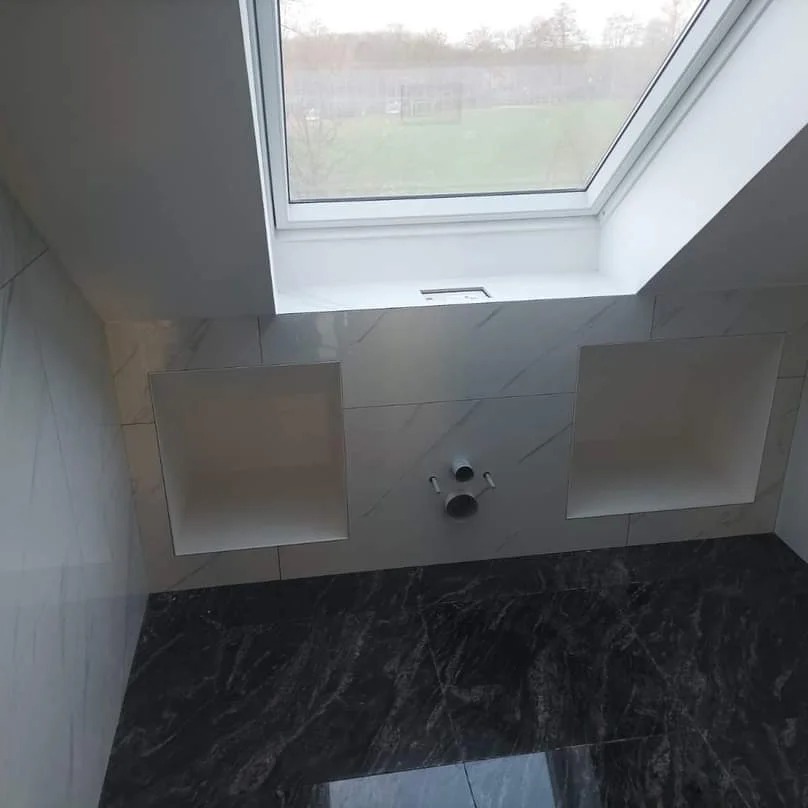 Łazienka na poddaszu z oknem dachowym i marmurowymi płytkami. Wykończone wnęki w ścianie. Czarna marmurowa podłoga. Minimalistyczny styl.