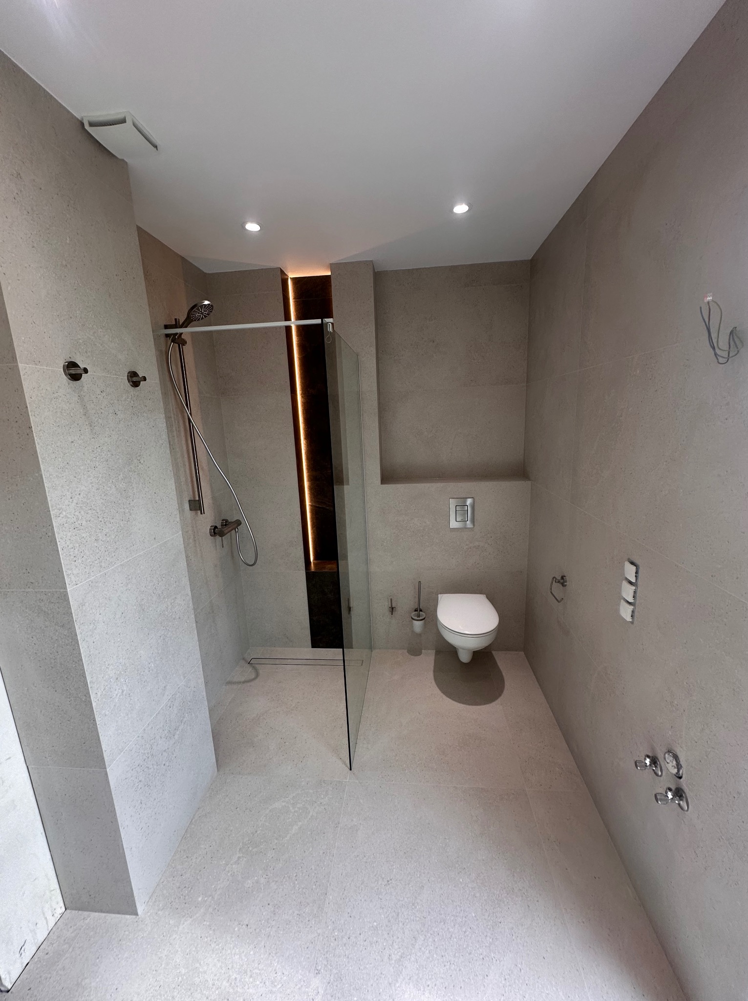 Nowoczesna łazienka w jasnych odcieniach szarości z kabiną prysznicową typu walk-in i podświetleniem LED. Minimalistyczny design z wiszącą miską WC.