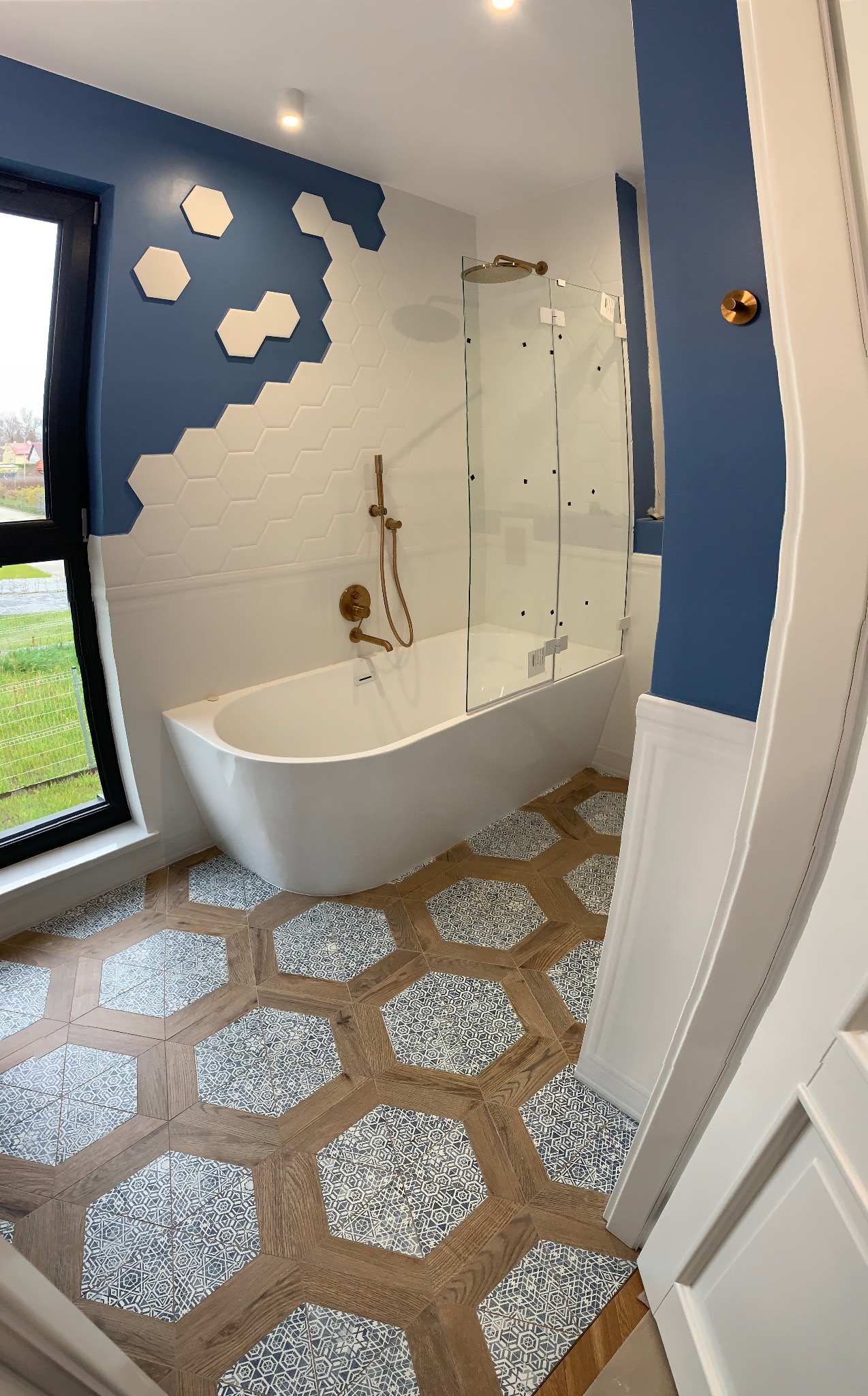 Nowoczesna łazienka z wanną, kabiną prysznicową i heksagonalnymi płytkami na ścianach oraz podłodze. Niebiesko-białe akcenty kolorystyczne.