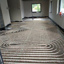 HYDROLUX MARCIN FELUKS - Rozłożona instalacja ogrzewania podłogowego w nowym budynku, widoczne rury na folii z siatką, okna w tle, surowy stan.