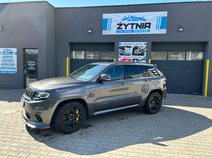 Szary Jeep Grand Cherokee po detailingu, zaparkowany przed myjnią Zytnia Car Wash, z widocznymi czarnymi felgami i żółtymi zaciskami hamulcowymi.
