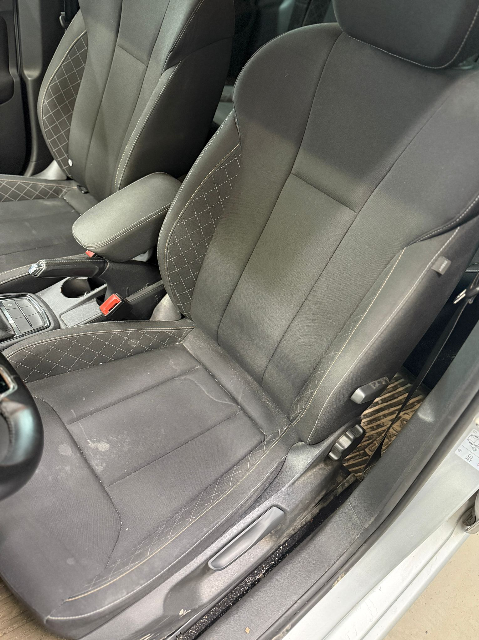 Zabrudzone, czarne siedzenie samochodowe z jasnymi przeszyciami, widoczne plamy i zanieczyszczenia na tapicerce. Detal wnętrza auta przed czyszczeniem.