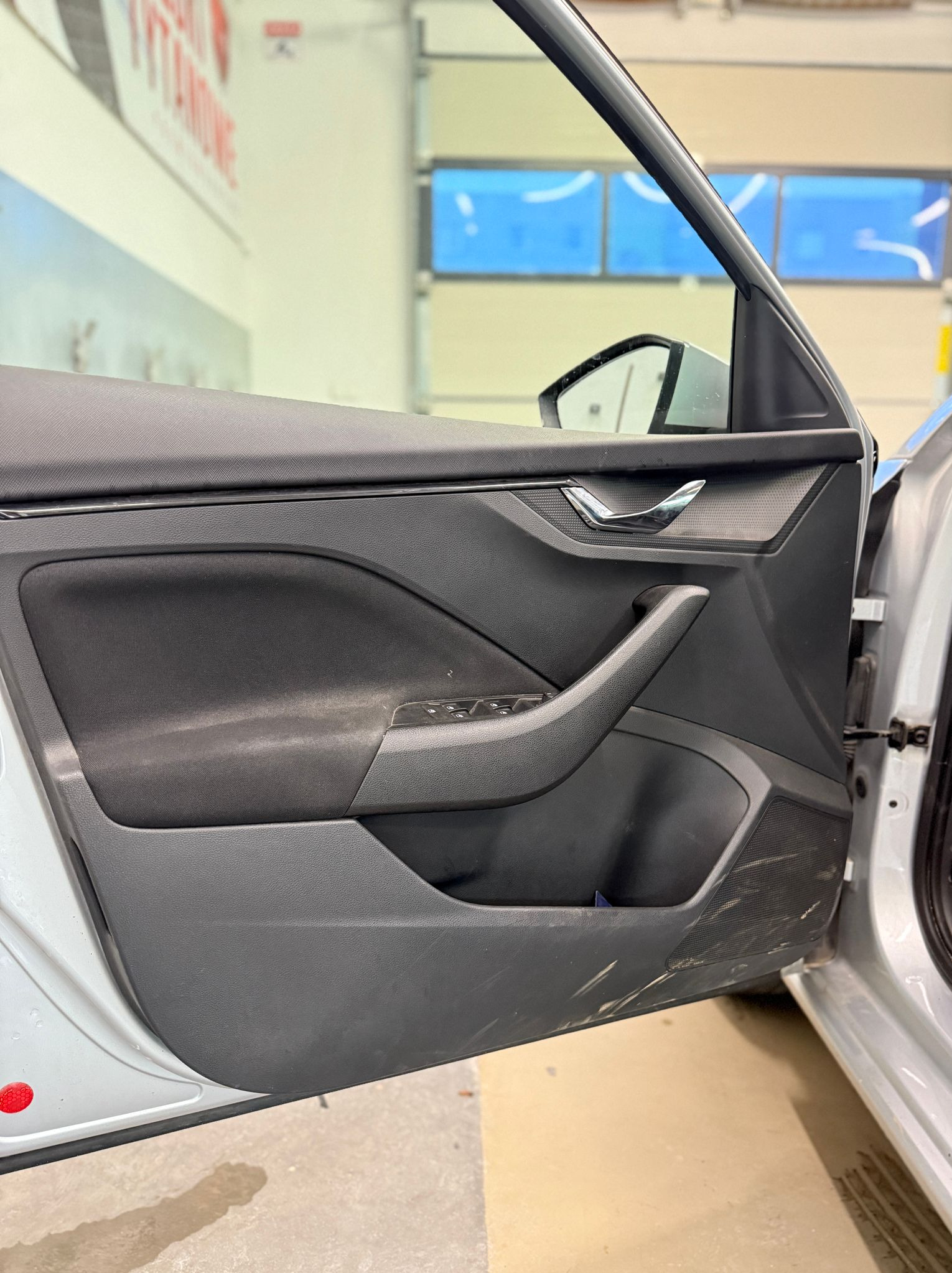 Wnętrze samochodu z otwartymi drzwiami, widoczny panel drzwiowy z elementami sterowania szybami i klamką, wnętrze auta wymaga czyszczenia.