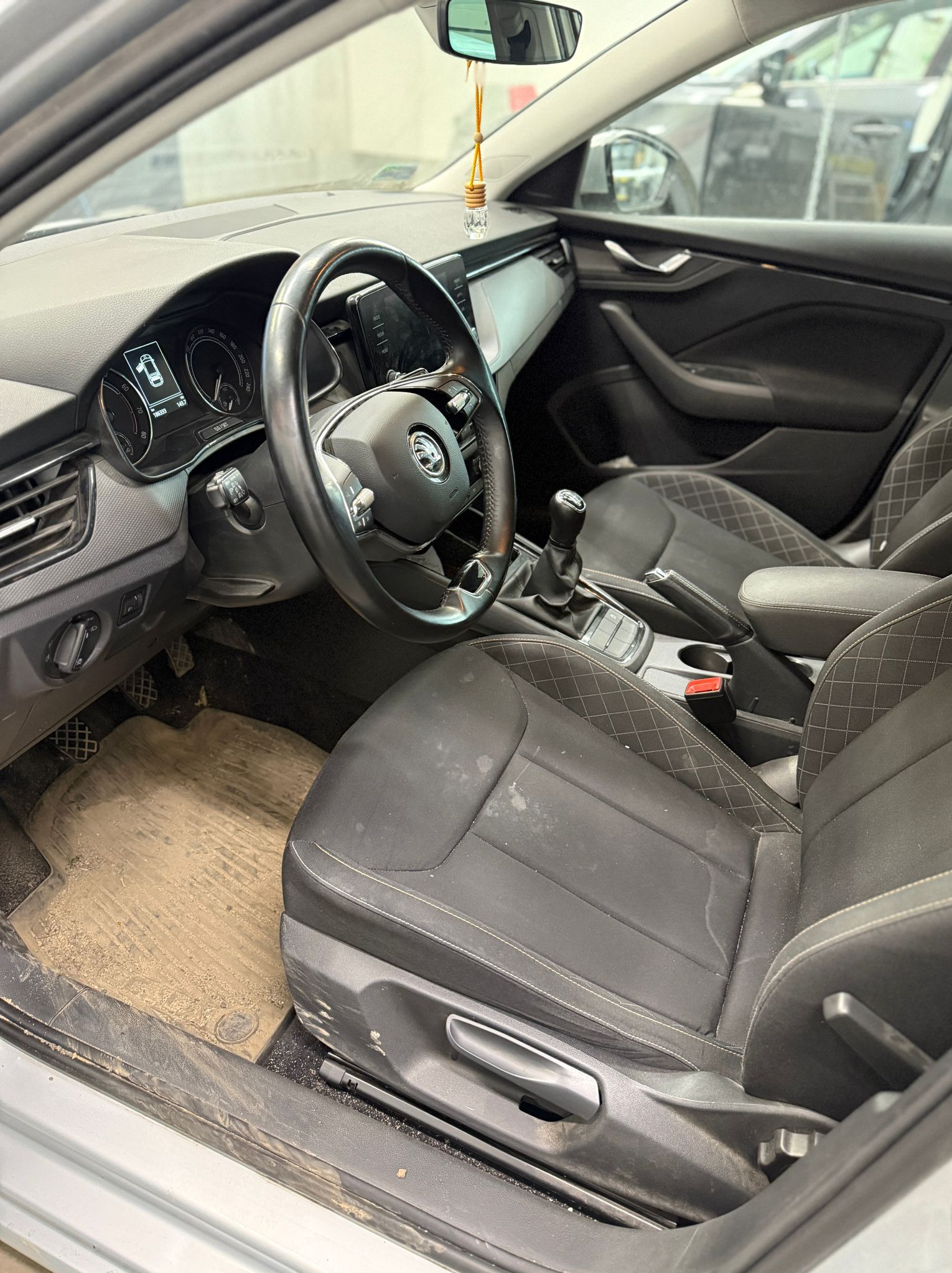 Wnętrze samochodu Skoda z wyraźnie zabrudzoną tapicerką i dywanikami, widoczne plamy i kurz. Kierownica i deska rozdzielcza również wymagają czyszczenia.