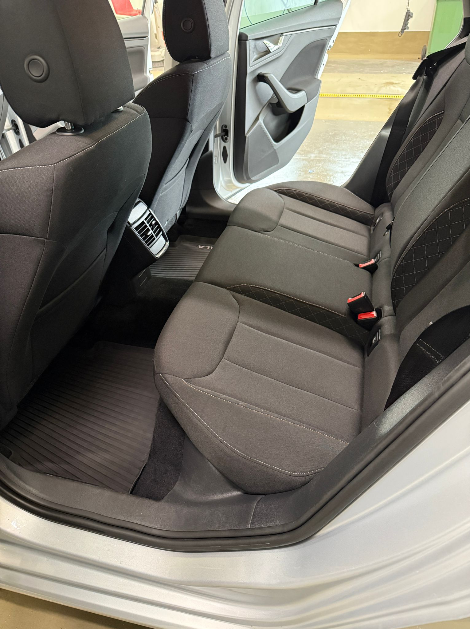 Wnętrze auta po praniu tapicerki w Koszalinie: czyste, ciemne fotele z jasnym przeszyciem, gumowe dywaniki i otwarte drzwi. Detale wykończenia.