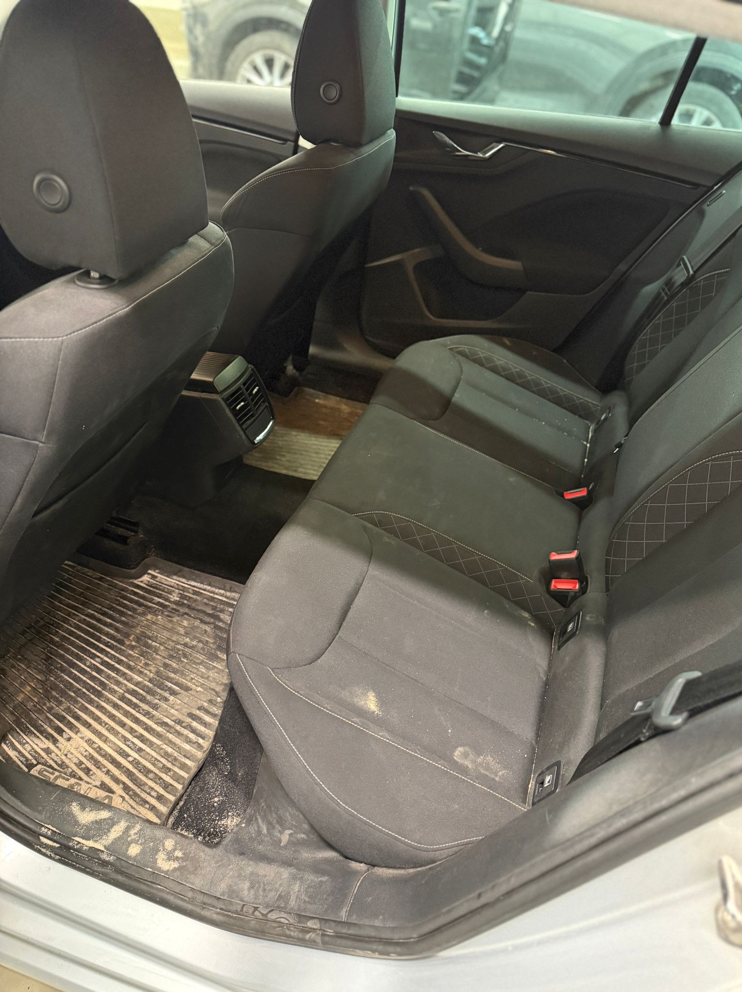 Brudne tylne siedzenia i dywaniki w samochodzie marki Skoda Octavia. Widoczne plamy i piasek. Potrzeba gruntownego czyszczenia tapicerki i dywaników samochodowych.