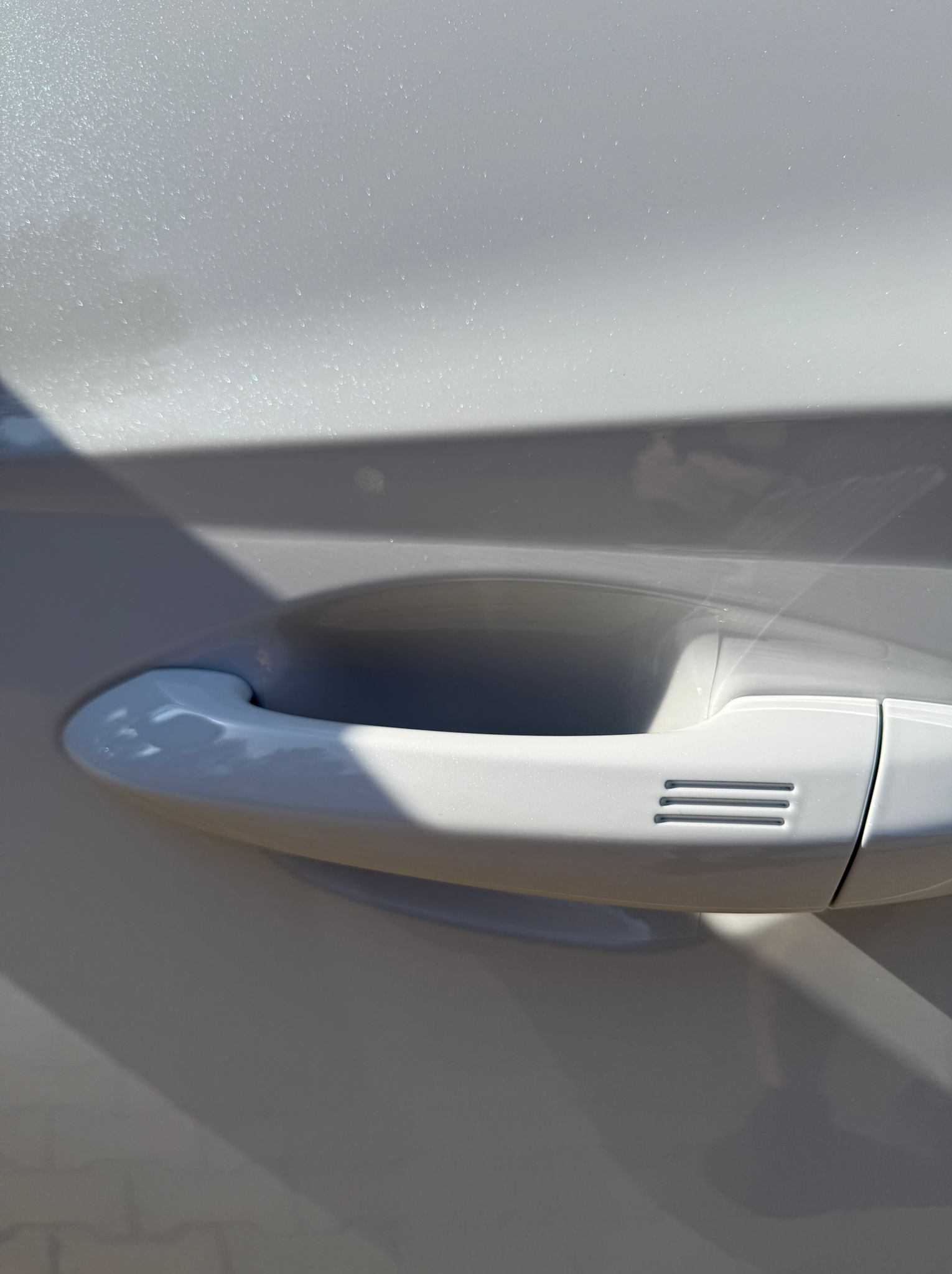 Błyszcząca, biała karoseria auta z chromowaną klamką w promieniach słońca. Widoczne refleksy i delikatne cieniowanie podkreślają czystość i dbałość o detale.