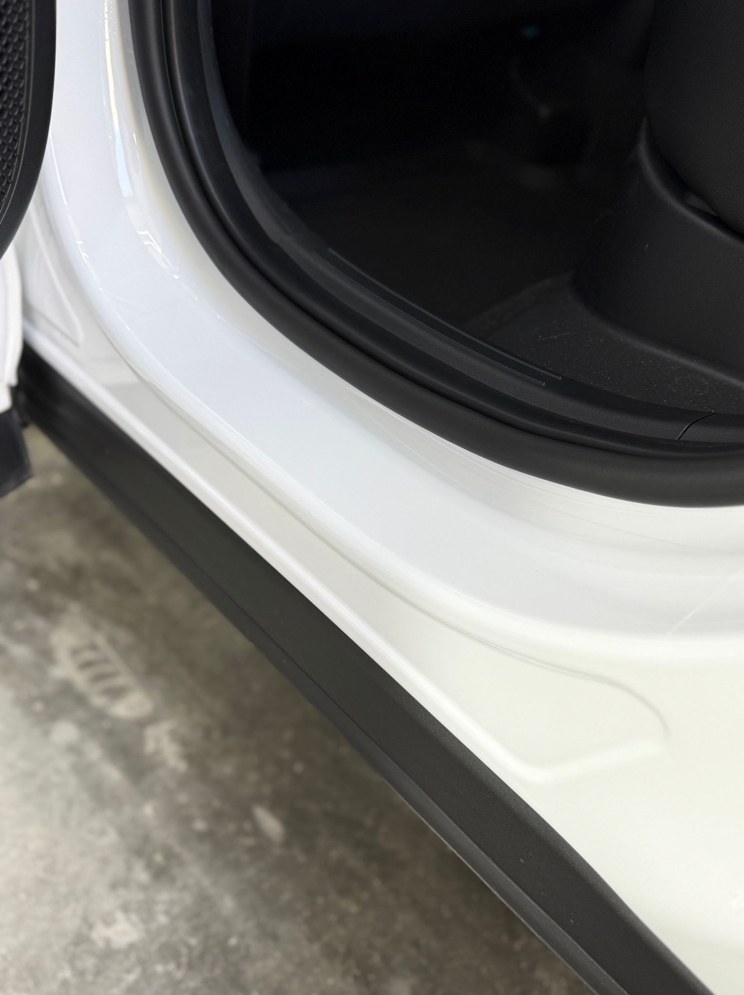 Wnętrze białego samochodu z widocznym progiem i uszczelką drzwi. Detal czystego, zadbanego wnętrza pojazdu z bliska.