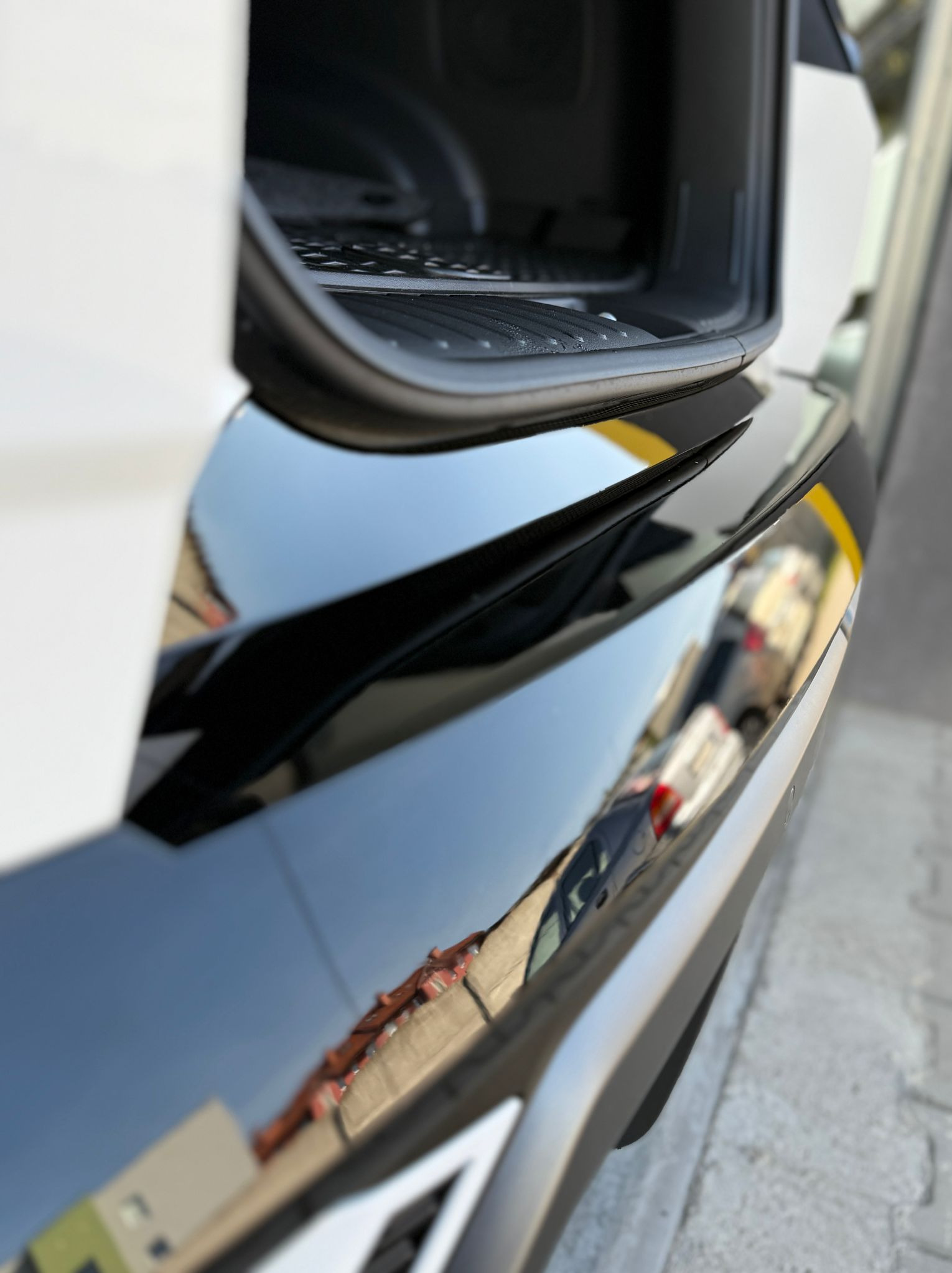 Błyszczący, czarny lakier na samochodzie z otwartym bagażnikiem, odbijający otoczenie. Widoczny fragment karoserii i wnętrze bagażnika.