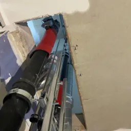 Montaż pionowych rur wentylacyjnych w otworze stropu, z widocznymi elementami mocującymi i izolacją termiczną na jednej z rur. Prace instalacyjne w surowym wnętrzu.