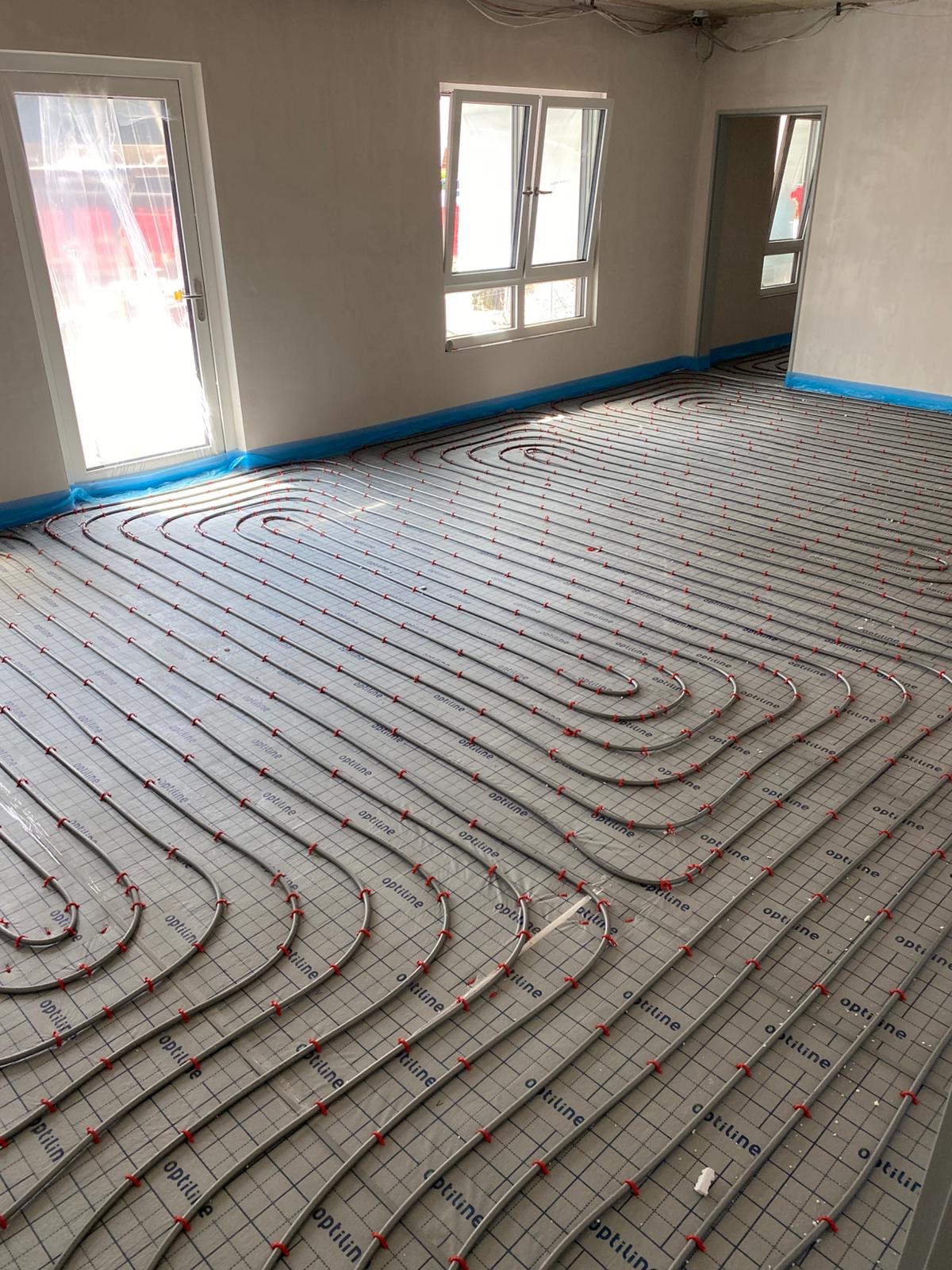 Ułożone rury ogrzewania podłogowego Optiline na izolacji, widok z góry, instalacja we Wrocławiu przed wylaniem posadzki. Nieotynkowane ściany i okno w tle.