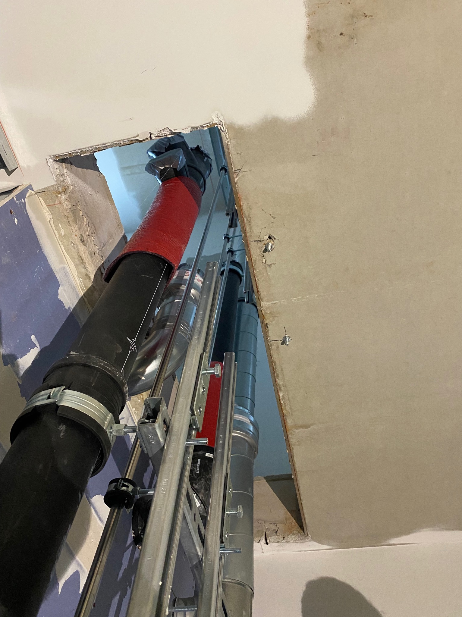 Montaż pionowych rur wentylacyjnych w otworze stropu, z widocznymi elementami mocującymi i izolacją termiczną na jednej z rur. Prace instalacyjne w surowym wnętrzu.