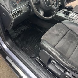 Mobilna Myjna SV - Wnętrze Audi A6 z czarnymi gumowymi dywanikami i szarymi fotelami z alcantary. Widoczne ślady użytkowania na fotelu kierowcy i czysta podłoga.
