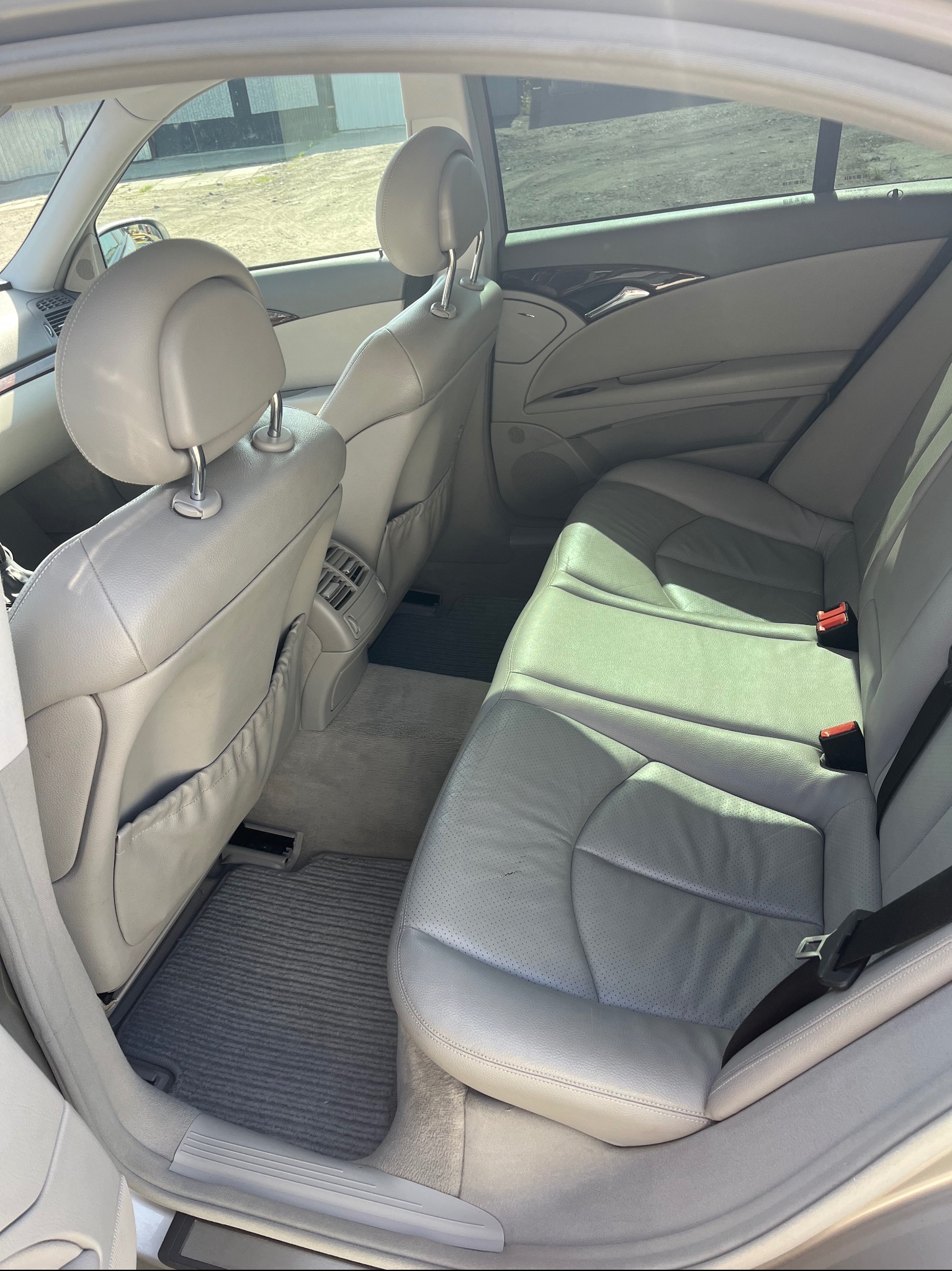 Wnętrze samochodu z szarą skórzaną tapicerką, widok na tylne siedzenia i dywaniki. Czyste i zadbane wnętrze pojazdu.