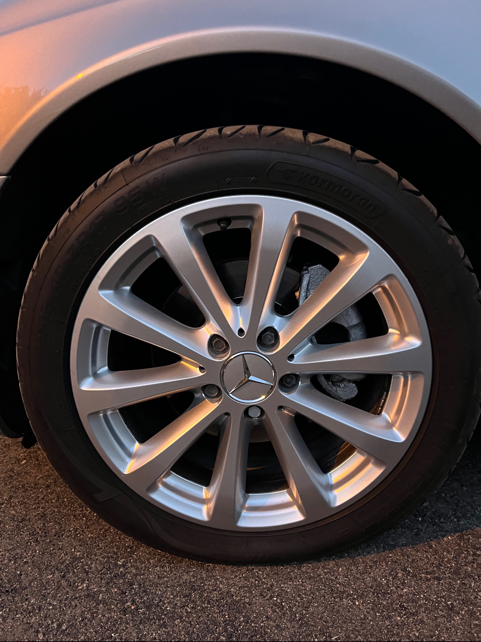 Błyszcząca felga aluminiowa marki Kormoran na oponie samochodu osobowego, z widocznymi zaciskami hamulcowymi i logo Mercedes-Benz na tle asfaltu.