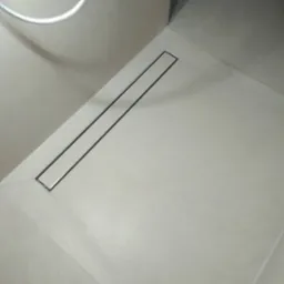 Minimalistyczna łazienka z odpływem liniowym w posadzce, wykończona jasnymi płytkami. Ujęcie z góry, widoczny fragment baterii prysznicowej.