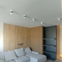 Jolanta Olczyk JR Prestige Meble - Minimalistyczny salon: narożnik w odcieniach szarości, drewniana ściana z lamelami i półki w zabudowie. Oświetlenie punktowe sufitowe.