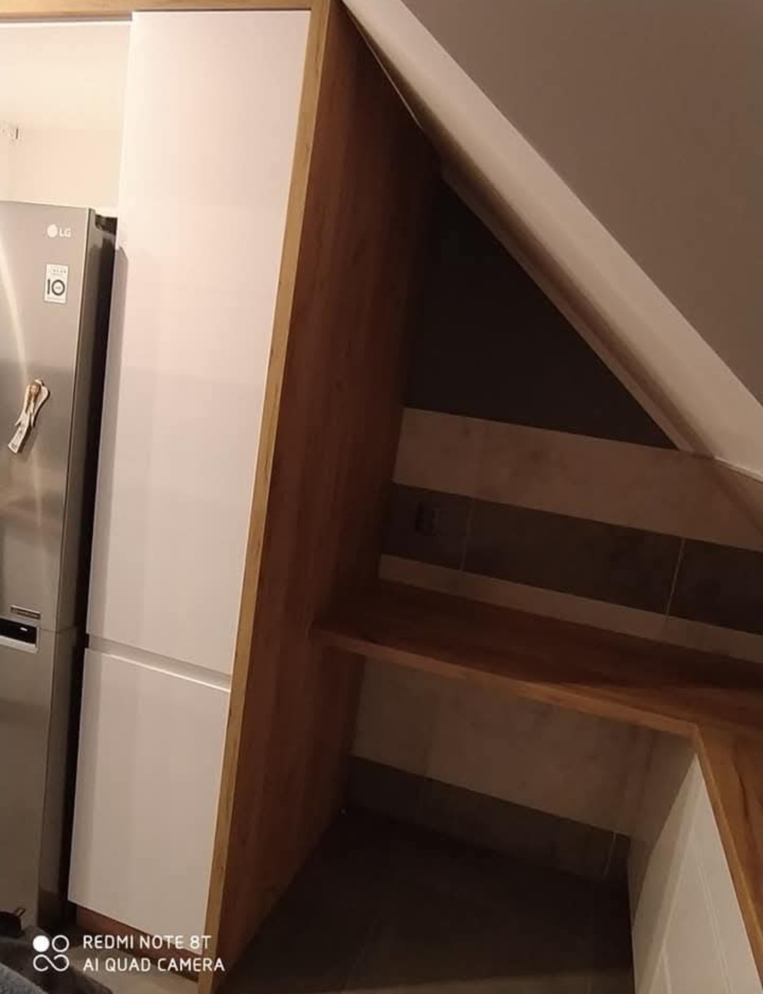 Kuchnia na wymiar: zabudowa w skosie z drewnianymi elementami i białą szafką, obok lodówka. Wykorzystanie przestrzeni pod skosami na funkcjonalną kuchnię.