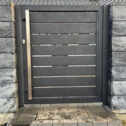 SteelCraft Andrii Hodziur - Nowoczesna, pozioma brama wjazdowa z szarego metalu, z prostokątnym uchwytem ze stali nierdzewnej, osadzona w słupkach z szarej kostki betonowej. Widok z bliska.