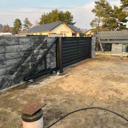 SteelCraft Andrii Hodziur - Nowoczesna, przesuwna brama wjazdowa z poziomymi panelami, zamontowana na tle szarego, betonowego ogrodzenia modułowego. Widoczne elementy mechanizmu bramy i teren w trakcie prac.