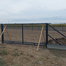 Usługi ogólnobudowlane Robert Chodkowski - Ciemnoszara, przesuwna brama panelowa w trakcie montażu, podparta drewnianymi stemplami. Widoczne betonowe fundamenty i przygotowany teren pod dalsze prace.