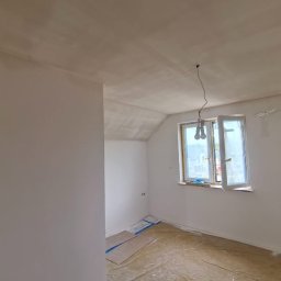 Aliaksej Kruty - Pokój po malowaniu: białe ściany, zabezpieczone okno folią malarską, podłoga zakryta kartonem i folią. Widoczne gniazdka elektryczne. Wnętrze gotowe do użytku.