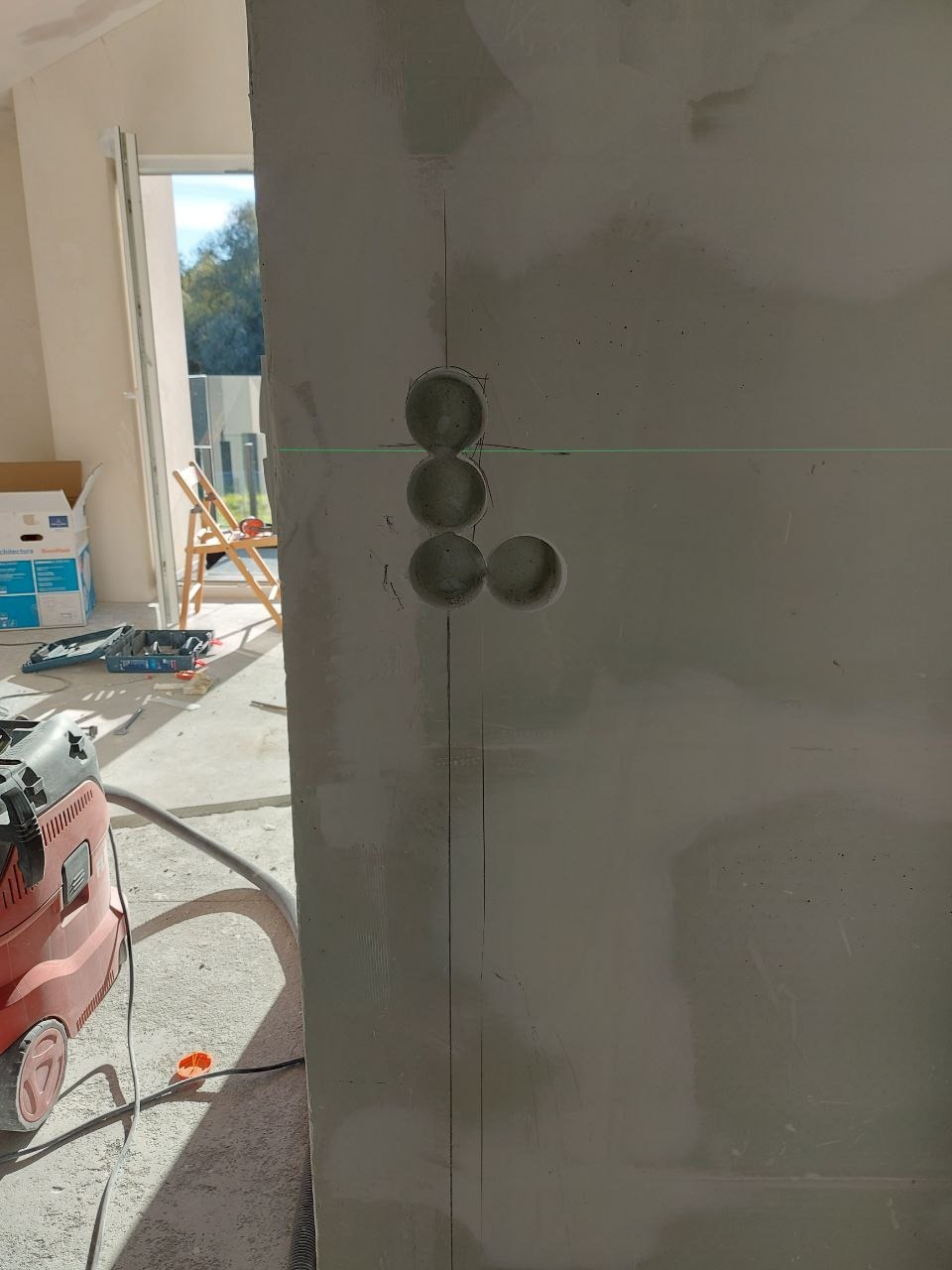 Przygotowanie ściany pod malowanie: wywiercone otwory na gniazdka elektryczne, widoczny laser krzyżowy, odkurzacz przemysłowy w Krakowie.