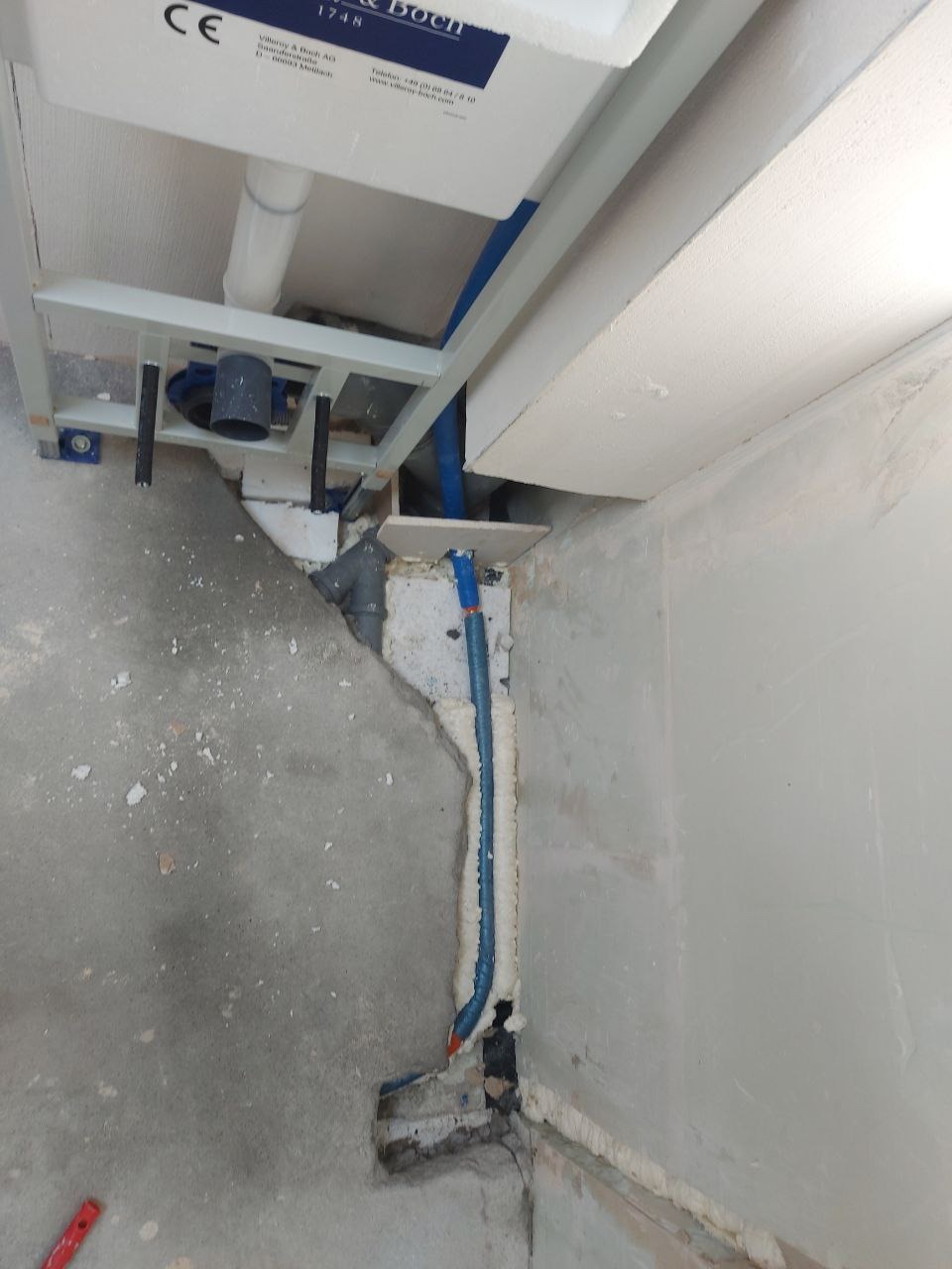 Narożne ujęcie surowej ściany z instalacją sanitarną, zabezpieczoną pianką montażową. Widoczne elementy stelażu podtynkowego. Stan surowy przed malowaniem.