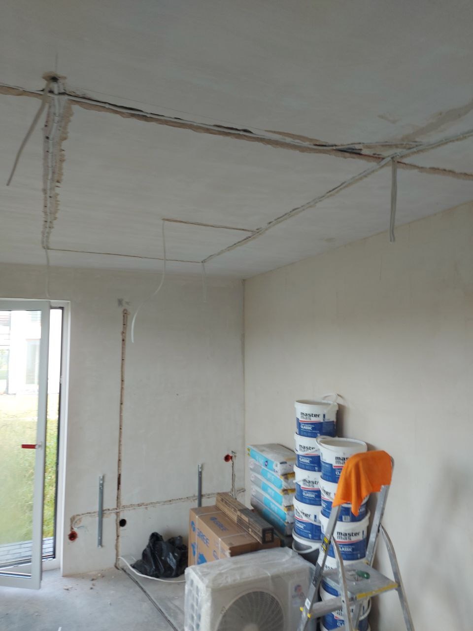 Przygotowanie do malowania: widoczne puszki z farbą, drabina, kable w bruzdach na suficie i ścianach, klimatyzator. Wnętrze w trakcie prac wykończeniowych.