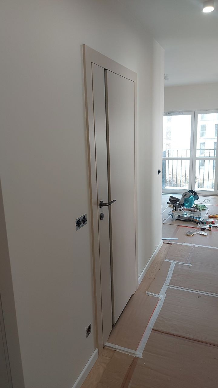 Jasne, świeżo pomalowane ściany w mieszkaniu z nowoczesnymi drzwiami i widocznymi puszkami elektrycznymi, przygotowane do dalszych prac wykończeniowych.