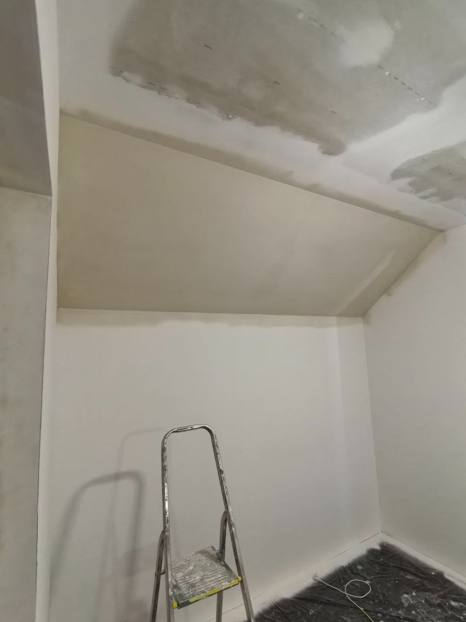 Świeżo zagruntowane ściany i sufit w pokoju, przygotowane do malowania. Widoczna drabina malarska. Podłoga zabezpieczona folią.