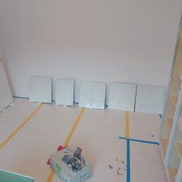 USŁUGI BUDOWLANE Krzysztof Gołębiowski - Przygotowane płyty do malowania w pomieszczeniu z zabezpieczoną podłogą. Widoczny kufer z narzędziami i malowane regały.