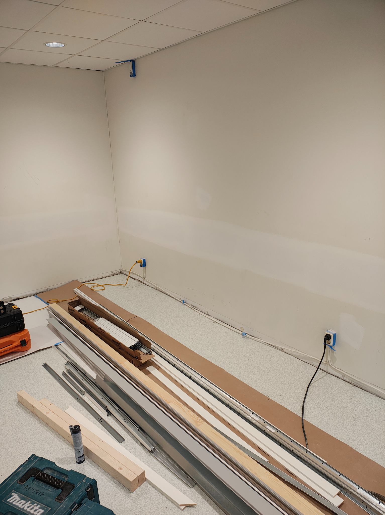 Przygotowanie do montażu listew przypodłogowych i sufitowych. Widoczne narzędzia i materiały budowlane w jasnym pomieszczeniu z pomalowanymi ścianami.