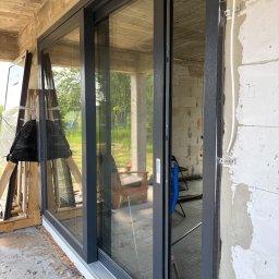 Drutex Susz - Montaż okna przesuwnego w surowym stanie. Widoczne profile okienne, pianka montażowa i elementy instalacji elektrycznej na ścianie z betonu komórkowego.