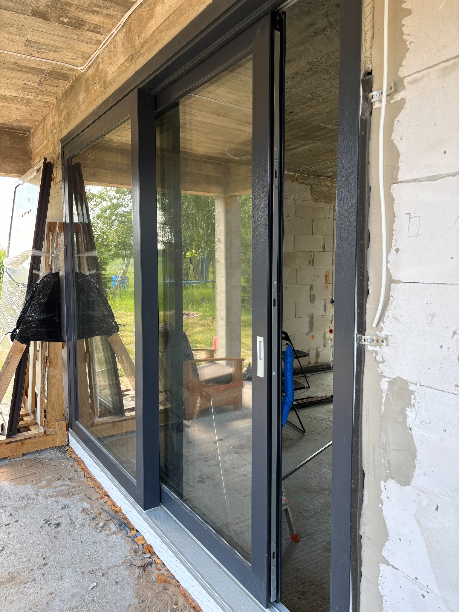 Montaż okna przesuwnego w surowym stanie. Widoczne profile okienne, pianka montażowa i elementy instalacji elektrycznej na ścianie z betonu komórkowego.